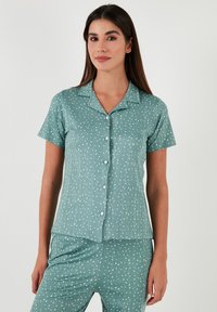 Pajama set kratkih rukava s ovratnikom u svijetlozelenoj boji s teksturiranim materijalom, s bijelim točkastim uzorkom i zatvaranjem na gumbe sprijeda.