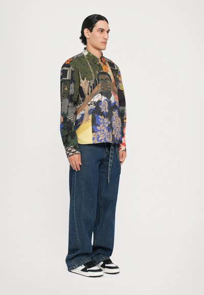 Langärmliges Hemd mit bunten grafischen Mustern, kombiniert mit lässigen blauen Jeans und schwarz-weißen Sneakern.