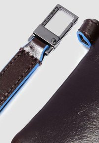 Dark brown leather bag strap with blue accents and meticulous stitching. Featuring a silver metal buckle with a rectangular shape.