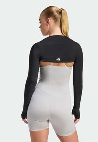 Czarna sportowa bluzka z długim rękawem z wycięciem na plecach, zestawiona z szarymi krótkimi body; gładka faktura i dopasowany fason.