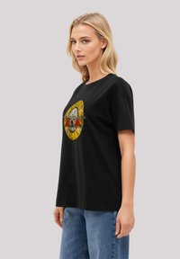 Black cotton t-shirt featuring a central graphic with a yellow circular design, skull, and red roses. Relaxed fit with short sleeves.