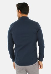 Camicia a maniche lunghe blu navy, design aderente con dettagli in bottone, tessuto liscio e yoke posteriore per una struttura e una vestibilità aggiuntive.