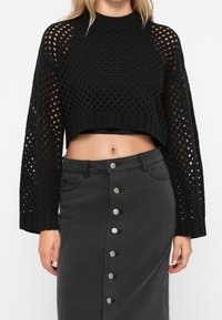Pull en maille noir raccourci à tissage ouvert, à col rond et à manches longues, associé à une jupe en denim noir taille haute avec des détails de boutons.