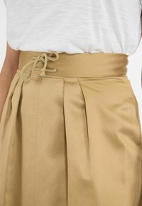 Jupe plissée kaki avec une taille haute et un détail à cordon de serrage, fabriquée en tissu lisse. Présente des plis verticaux et une couleur unie.