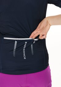 Marine atletisk skjorte med reflekterende detaljer, der har en baglomme. Glat tekstur, tætsiddende design og strækbart stof, parret med lilla shorts.