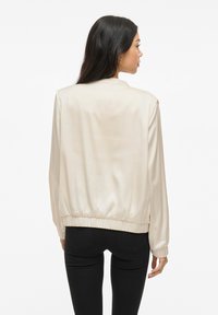 Ljust beige bomberjacka med en slät, glänsande yta, elastiska cuffs och nederkant, med en avslappnad passform och enkel design.