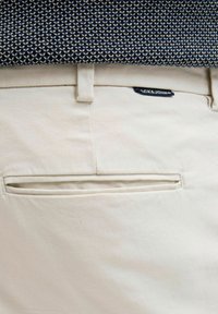 Beige bomuldsbukser med en baglomme med et mærke. Stoffet har en glat tekstur og struktureret design med en lige pasform.