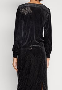 Svart sammetsklänning med långa puffärmar, med subtila prickiga mönster, sidofåra och slät textur. Bakifrån visas en avslappnad passform.