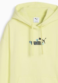 Žltá mikina s kapucňou a predným vreckom, so športovým čiernym logom a kvetinovými detailmi. Je vyrobená z mäkkého materiálu, s šnúrkami a klokankovým vreckom.