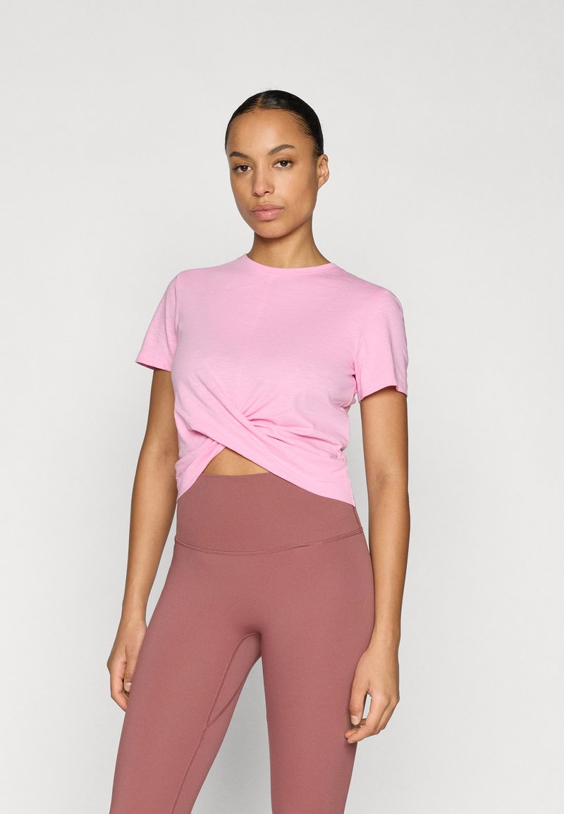 Ροζ κοντομάνικη μπλούζα με στριφογυριστό σχέδιο στο μπροστινό μέρος, κατασκευασμένη από μαλακό ύφασμα. Συνδυασμένη με ψηλόμεσο, στενόκαρδο καφέ κολάν.