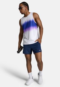 Biały top na ramiączkach z purpurowym ombre, w połączeniu z granatowymi szortami. Modelka trzyma hantel, nosząc okulary przeciwsłoneczne i białe buty sportowe.