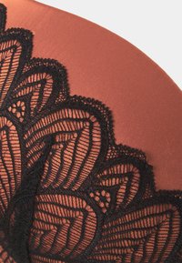 Lingerie en tissu lisse de couleur rouille, mettant en valeur un délicat motif en dentelle noire le long du bord supérieur, avec des motifs floraux et une bordure festonnée.