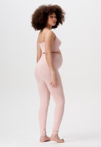 Ensemble de maternité rose pâle comprenant un haut cropped ajusté à côtes et des leggings taille haute avec des poignets de cheville serrés. Texture douce, design minimaliste.