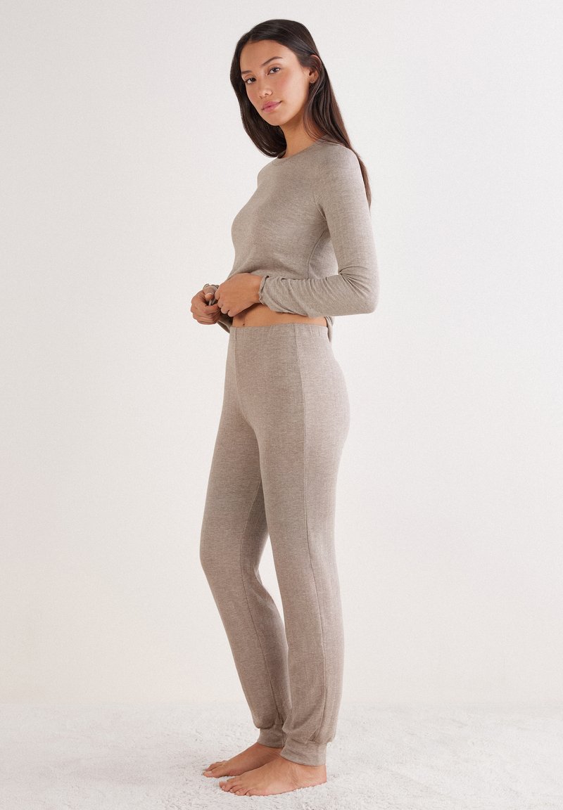 Beige Langarmoberteil und passende Hose aus einem weichen, strukturierten Stoff. Das Oberteil hat einen runden Ausschnitt und taillierte Ärmel, während die Hose eine schmal zulaufende Passform hat.