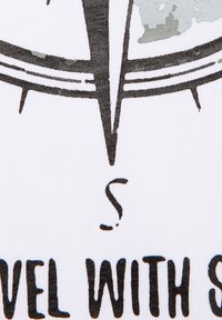 Biała tkanina z wyraźnym, czarnym wzorem kompasu, z literą 'S' oraz frazą "PODRÓŻUJ Z" w czarnym tekście poniżej.