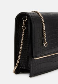 Czarna torebka ze skóry wegańskiej o strukturze krokodylej, z złotym łańcuszkiem i zapięciem. Charakteryzuje się minimalistycznym designem oraz poziomym złotym akcentem.