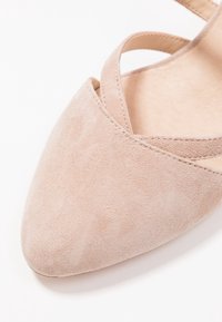 Zapato de ante rosa claro con punta afilada y diseño de tiras entrecruzadas. Textura suave y detalles de costura mínimos.