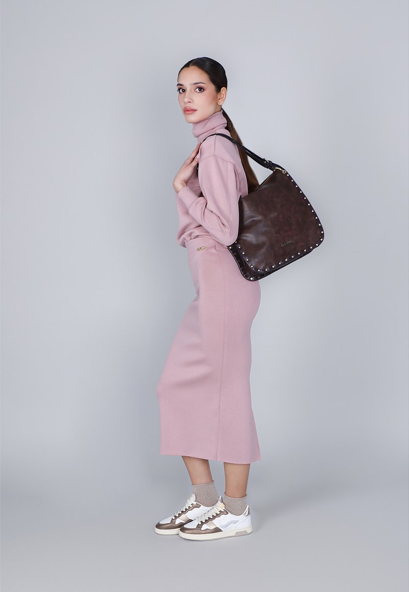 Roze gebreide coltrui en midi rok outfit met een bruine leren tas met studs, gecombineerd met witte sneakers en beige sokken.