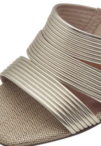 Metallic gold sandal with multiple textured stripes and a woven beige outsole. Soft inner lining and open design.