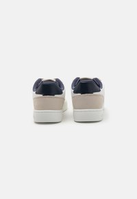 White sneakers with navy and beige accents, textured upper materials, round toe, and padded collar, designed for comfort and style.