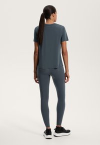 Sötétszürke sportpóló rövid ujjakkal, hozzá illő, szoros szabású leggings-szel. Az anyag sima és rugalmas; minimális dizájn részletek.