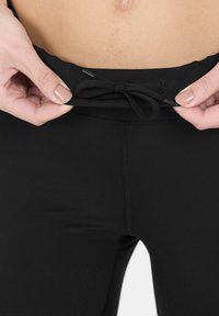 Svarta sportleggings med en slät yta, med dragsko i midjan och sömnadsdetaljer längs sidorna.