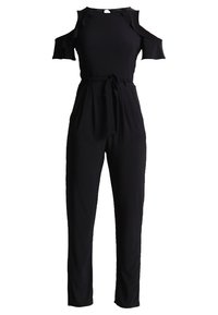 Combinaison noire avec découpes épaules dénudées, manches courtes, taille ceinturée et pantalon long fuselé sur fond blanc.