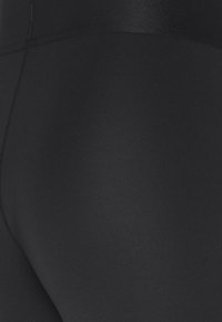 Leggings noirs à texture lisse et mate avec une taille haute. Le design est sans coutures avec une couleur uniforme partout, sans motifs ni accents.