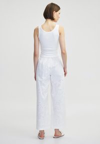 Weißes Tanktop kombiniert mit weißen weit geschnittenen Hosen mit floralen Lochstickereien. Das Outfit zeigt ein schlichtes, sauberes Design und eine leichte Textur.