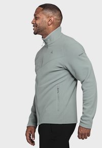 Hellgrüner Fleece-Jacke mit hohem Kragen, Frontreißverschluss und Seitentaschen. Verfügt über eine glatte Textur und ein dezentes Logo auf der Schulter.