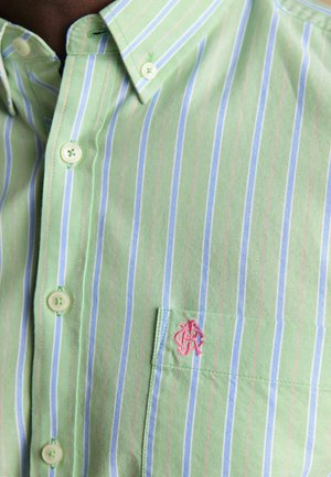 Artimos žalios spalvos marškiniai su vertikaliomis mėlynomis ir rožinėmis juostelėmis, kišenėje yra mažas siuvinėtas rožinis logotipas.