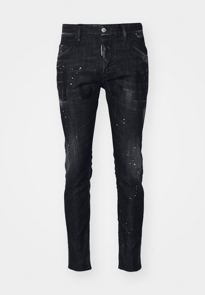 Mustad denim teksad, millel on kitsas lõige, kulunud tekstuur, värvilaigud ja julged graafilised printides ees.