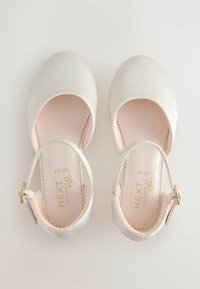 Valkoiset nahkaiset balettitossut nilkkaremillä, pyöreällä kärjellä ja aaltoilevalla sisäpohjallisella. Kultaiset metalliyksityiskohdat remmissä.