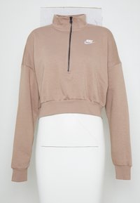 Brun beskuren pullover med hög krage, halvdragkedja framtill, långa ärmar och en vit Nike-logotyp på vänster bröst. Mjuk tygtextur.