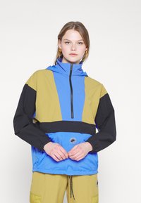 Fargeblokkerte vindjakker med design i blått, svart og olivengrønn; har høy krage, halv-zip front og stramme mansjetter.