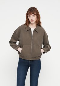Veste bomber en velours côtelé vert olive avec fermeture éclair à l'avant, col et poignets élastiques. Dotée de poches latérales et d'une coupe décontractée.