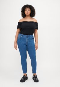 Black off-the-shoulder top with pleated details paired with high-waisted blue jeans and chunky black platform shoes.