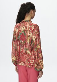 Durchsichtige, gemusterte Bluse mit rundem Halsausschnitt und puffigen Ärmeln in Rot-, Rosa- und Grüntönen, die Blumen- und geometrische Designs aufweist.