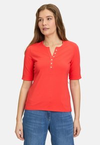 Rød kortærmet top med henley-udskæring, prydet med fem knapdetaljer. Fremstillet af et glat materiale med en tætsiddende pasform.