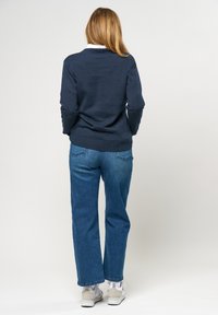 Marineblauwe gebreide trui met een geribde onderrand, gecombineerd met lichtblauwe recht-pasvorm jeans en witte sportschoenen.