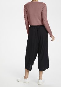 Różowy, krótki sweter z długimi rękawami, zestawiony z czarnymi, szerokimi spodniami culottes. Dodatkowo występują białe sneakersy. Gładka tekstura, casualowy fason.