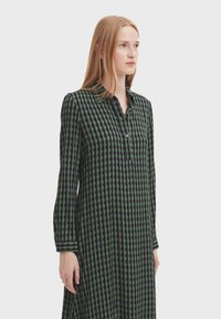 Long-sleeved dress in black and green with a geometric pattern. Features a collar and button placket, made from a smooth fabric.
