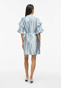 Abito azzurro chiaro con maniche arricciate, dettaglio della cintura e orlo decorato con forme geometriche. Realizzato in un tessuto liscio e leggero.