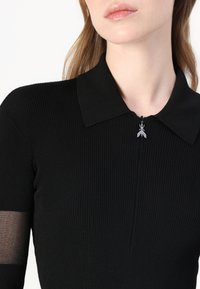 Top nero a costine con colletto, dotato di chiusura con zip e piccolo elemento metallico sul tirante della zip; maniche corte con pannelli trasparenti.