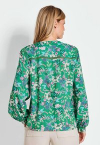 Groene bloemenblouse met lange mouwen, een ronde halslijn en een contrasterende decoratieve bies langs de achterste hals en schouders.