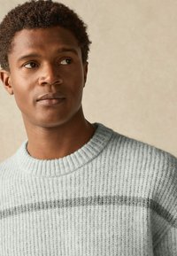 Light gray, ribbed sweater with a crew neckline and a dark gray horizontal stripe. Soft texture and relaxed fit.