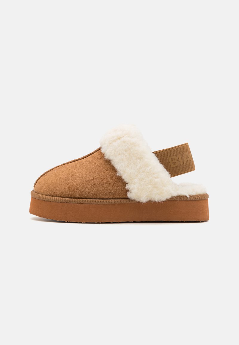 Brune semskede slip-on tøffel med hvit, fluffy fôr og gummisåle. Har en elastisk bakrem med "BIA" preget.