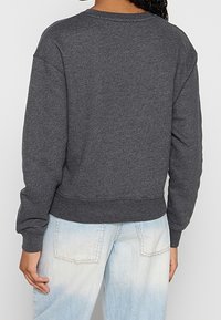 Maglione grigio a girocollo con polsini e orlo a costine, caratterizzato da una vestibilità comoda. Indossato sopra un paio di jeans azzurri chiari, leggermente sbiaditi.