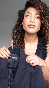 Blazer preto com textura suave, apresentando um design ajustado e lapelas nítidas, pendurado num cabide, com a etiqueta da marca visível no interior.