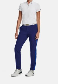 Vit pikétröja med kort ärm, matchad med marinblå byxor med blå sidostickningar och ett vitt bälte. Grå och svarta sportskor.